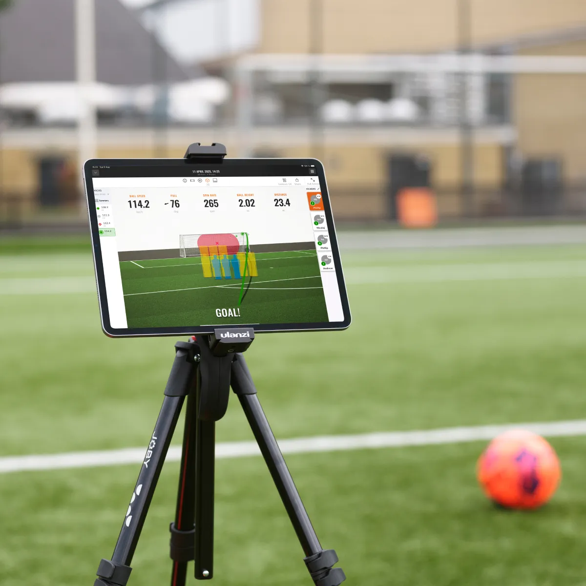 Tablet on a tripod displaying sports analytics on a soccer field, with scattered soccer balls and a goal in the background.